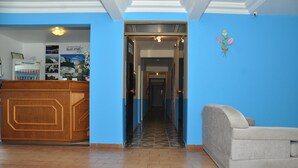 A reception area with a wooden counter, a blue wall, and a grey sofa. - Hotel Blue Star II (Foz do Iguacu)