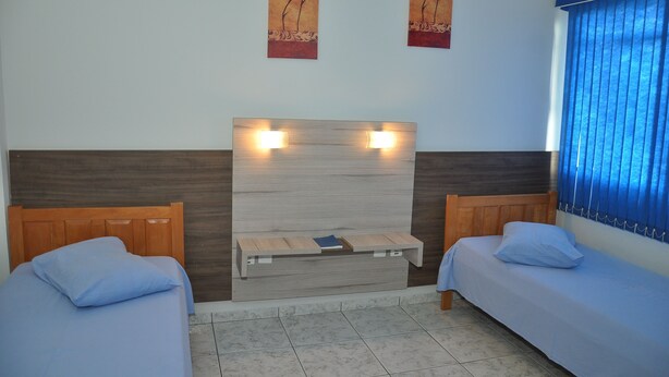 A hotel room with two single beds, a wooden headboard, a small wooden shelf, and two wall-mounted light fixtures. - Hotel Blue Star II (Foz do Iguacu)