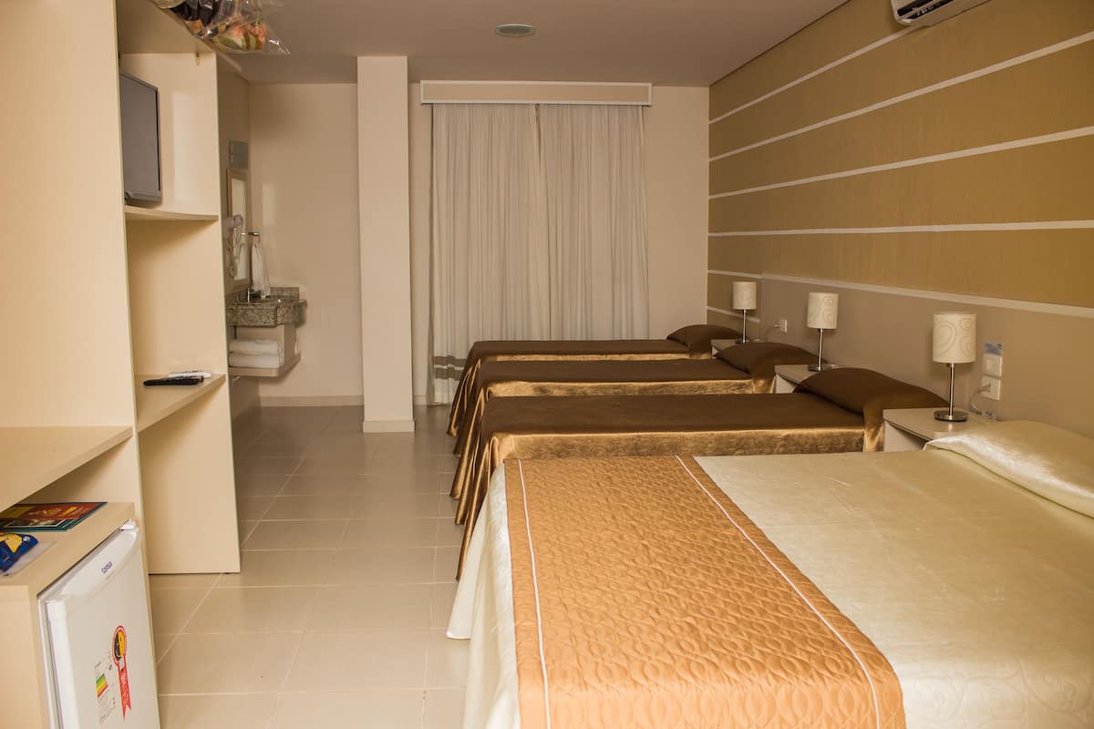 A hotel room with three beds, a desk, a refrigerator, and a bathroom with a shower and toilet.
