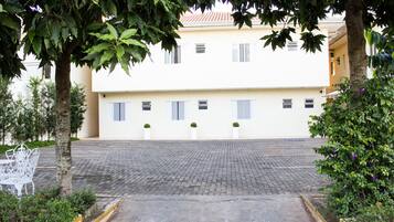 A courtyard with a paved walkway, a white bench, and a building with multiple windows and shutters.