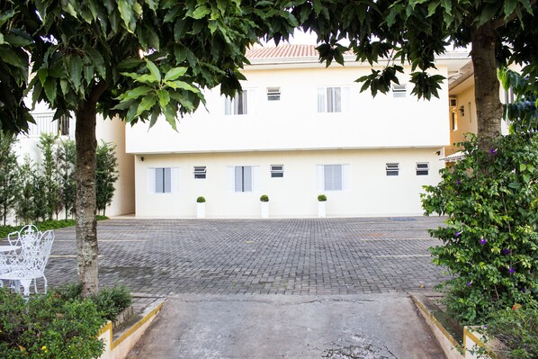 A courtyard with a paved walkway, a white bench, and a building with multiple windows and shutters. - Hotel e Pousada Cataratas (Foz do Iguaçu)