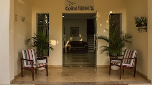 L'ingresso di un hotel con un cartello che riporta "Colibri Turismo LTDA". Ai lati dell'ingresso ci sono due piante in vaso e una porta in vetro che dà sull'interno.