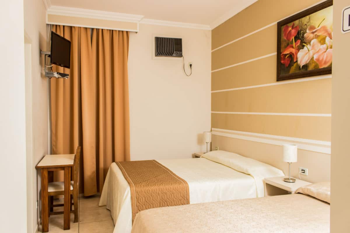 A hotel room with two beds, a desk, a chair, a painting on the wall, and a window with curtains.