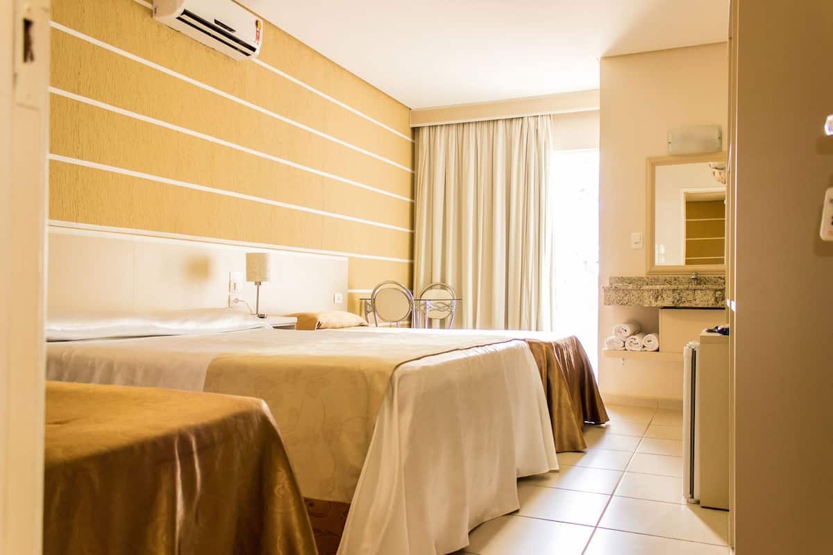 A hotel room with two beds, a small sitting area, a mirror, a radiator, and a kitchenette.