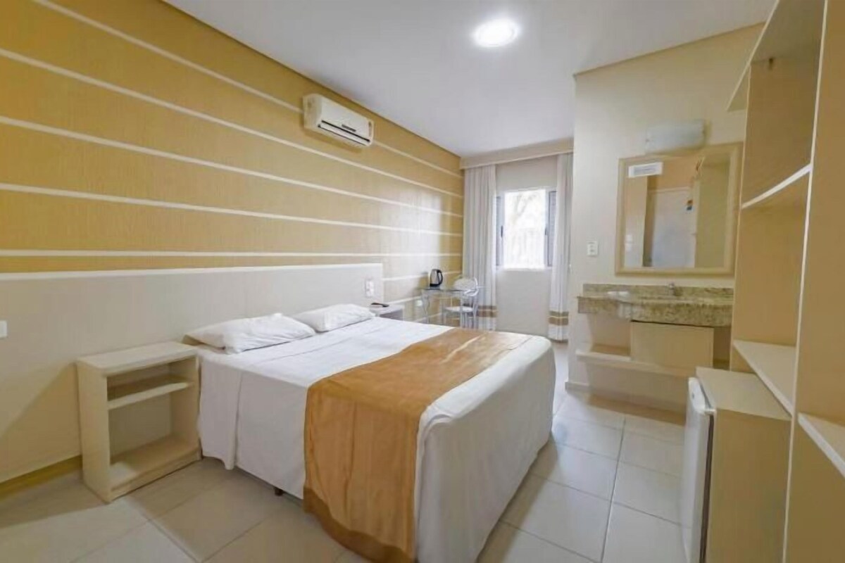 Une chambre d’hôtel comprenant un lit, une table de chevet et une salle de bain avec un lavabo et un miroir.