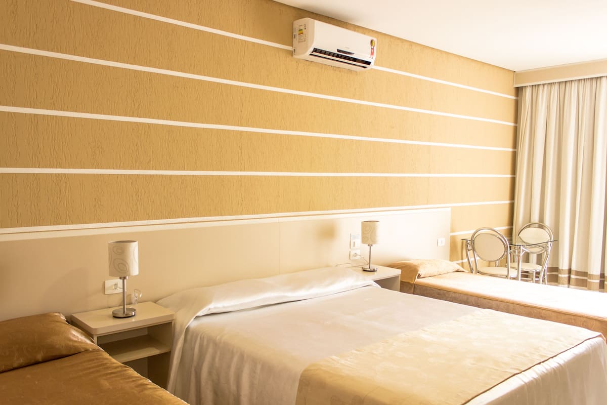 A hotel room with a bed, bedside tables, a mirror, and an air conditioning unit on the wall.