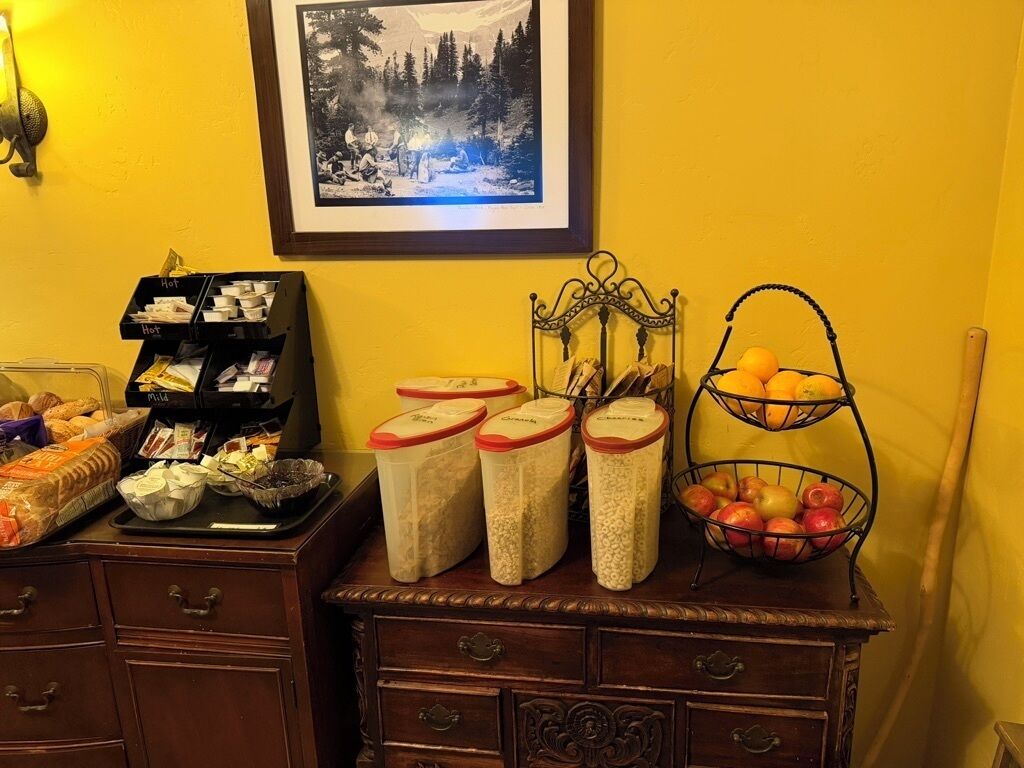 A kitchen counter with jars of grains, a basket of apples, and a tray of bread.