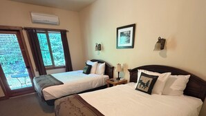 A hotel room with two beds, a large window, an air conditioning unit, and a framed picture on the wall. - Glacier Guides Lodge (West Glacier)