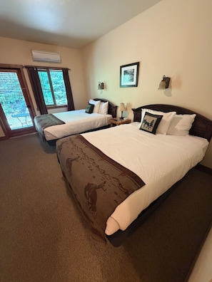 A hotel room with two beds, a large window, an air conditioning unit, and a framed picture on the wall.