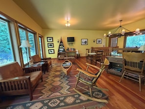 A cozy living room with a fireplace, wooden furniture, and a large window overlooking trees.