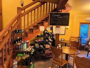 A cozy interior with a staircase, a wooden table, chairs, and shelves stocked with various items. - Glacier Guides Lodge (West Glacier)