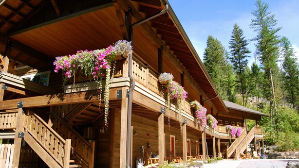 A wooden lodge with a covered porch, stone steps, and hanging flower baskets. - Glacier Guides Lodge (West Glacier)