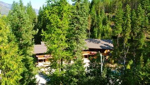 A lodge with a wooden exterior, surrounded by dense forest and mountains in the background. - Glacier Guides Lodge (West Glacier)