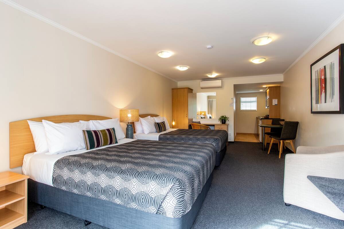 A hotel room with two beds, a desk, a chair, and a small kitchenette.