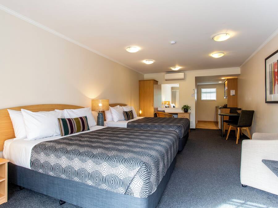 A hotel room with two beds, a desk, a chair, and a small kitchenette.