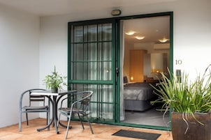 A room with a bed, a table with two chairs, a potted plant, and a sliding glass door leading to another room.