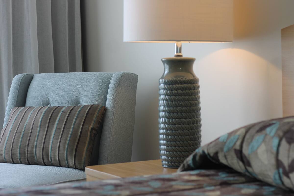 A neatly arranged hotel room with a sofa, a lamp, and a bed.