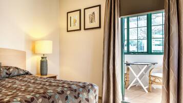 A hotel room with a bed, a lamp, two framed pictures on the wall, and a view of the outside through a window.