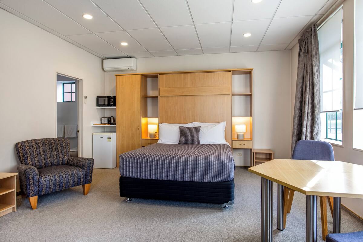 A hotel room with a bed, a desk, a chair, a wardrobe, and a microwave.