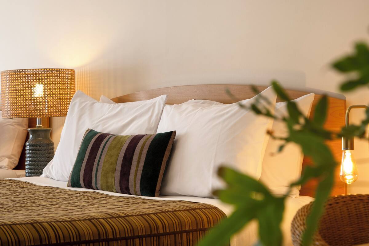 A neatly made bed with a striped pillow, a lamp, and a vase on the nightstand.