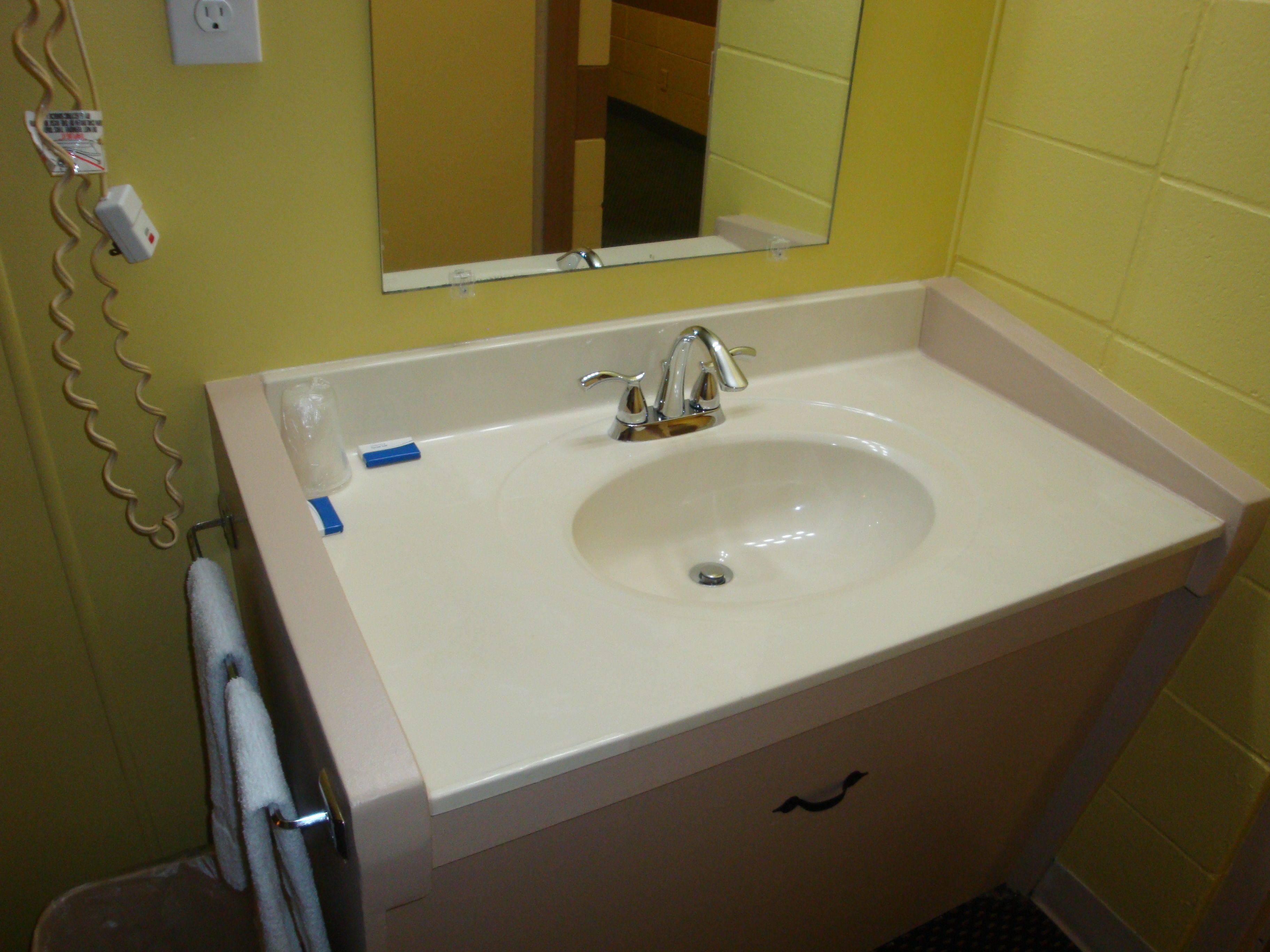 Un baño con un lavabo blanco, un espejo encima y una toalla colgada en un perchero.