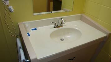 Un baño con un lavabo blanco, un espejo encima y una toalla colgada en un perchero.