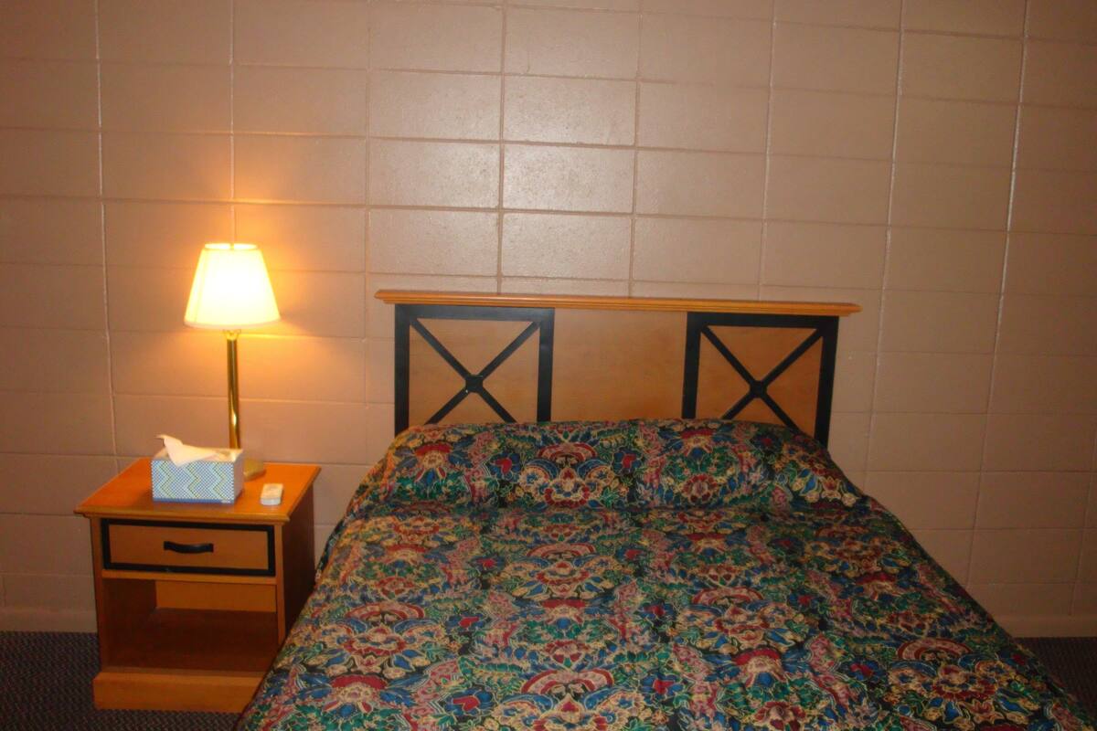 A bed with a patterned bedspread, a bedside table with a lamp, and a wall with a tiled pattern.