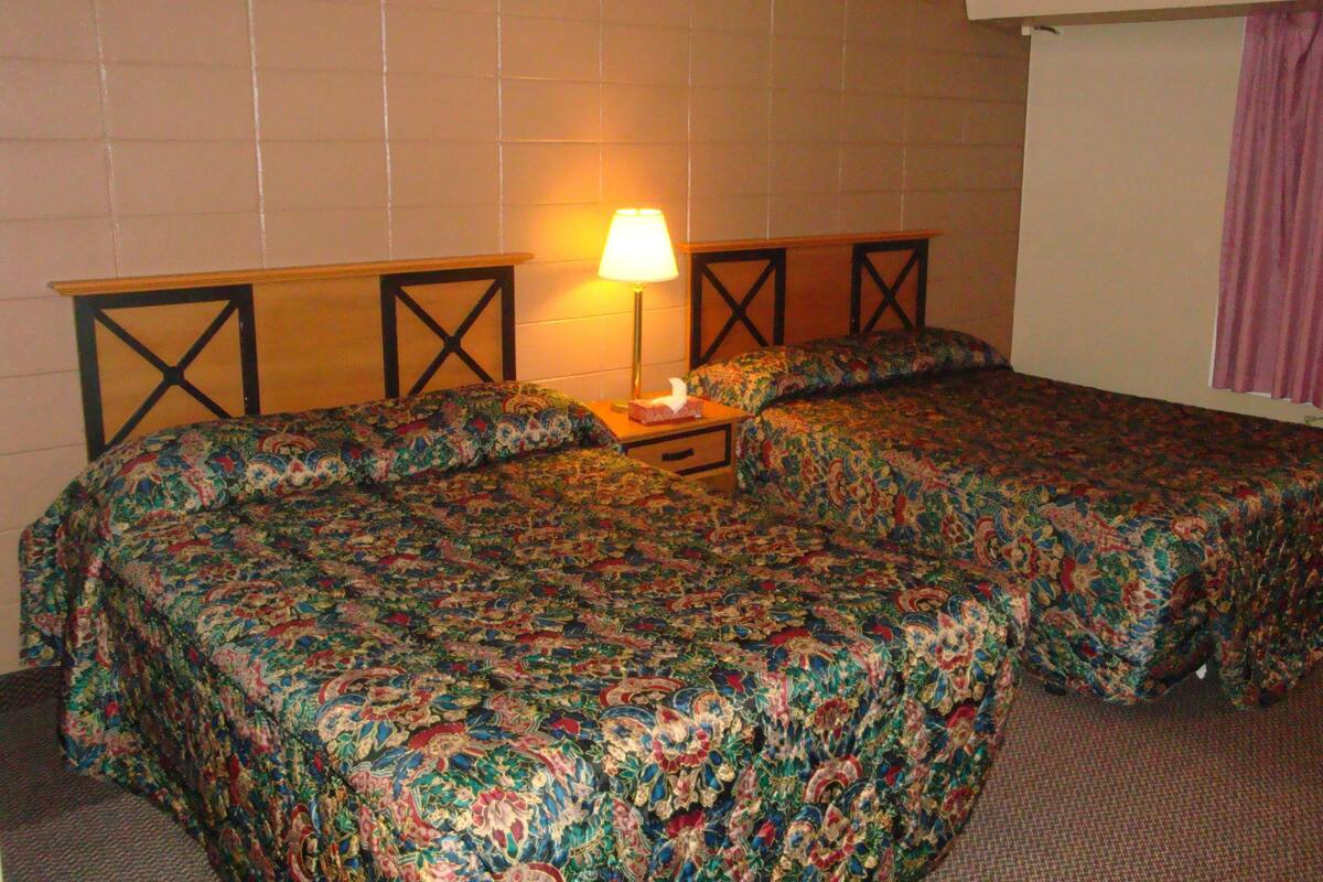 A room with two beds, a nightstand, a lamp, and a window with curtains.