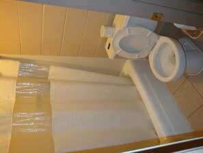 A bathroom with a toilet, a white shower curtain, and a white bathtub.