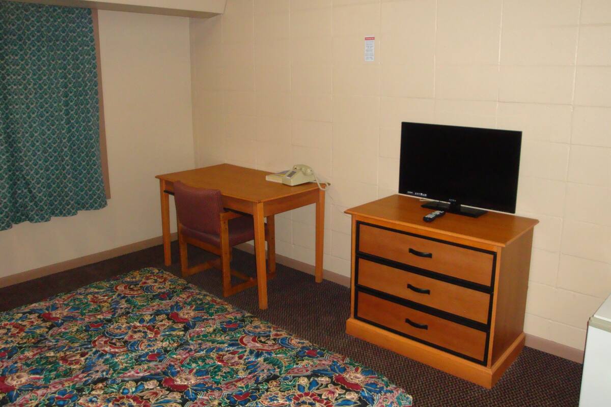 A small, simple room with a bed, a desk, a chair, a television, and a dresser.