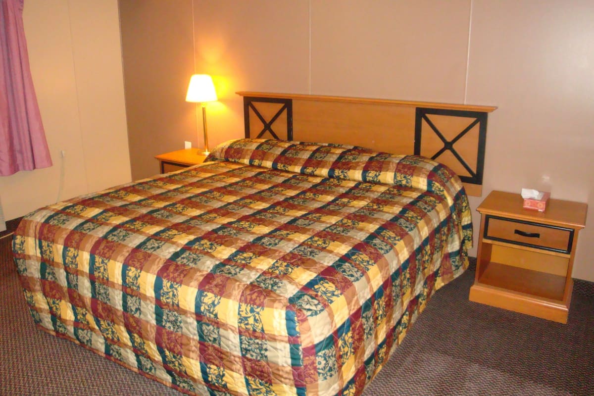 A hotel room with a large bed, a nightstand with a lamp, and a small drawer unit.