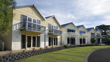 A row of modern townhouses with balconies, a stone retaining wall, and a well-maintained lawn.