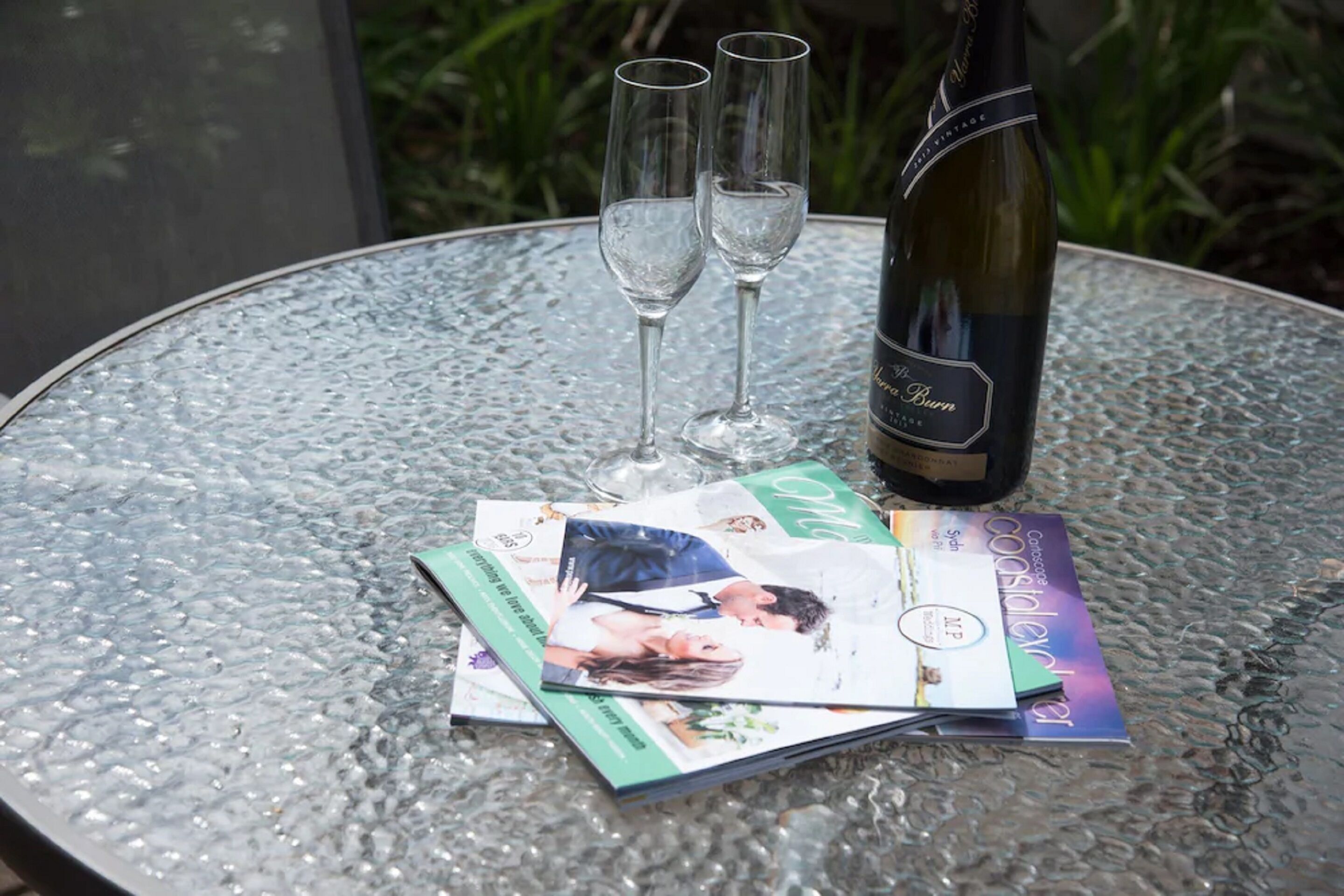 Une table avec une bouteille de vin, deux verres et plusieurs magazines.