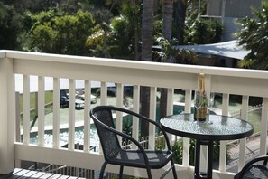 A balcony with a round glass table and two chairs, overlooking a pool and greenery. - Boathouse Resort Studios & Suites (Blairgowrie)