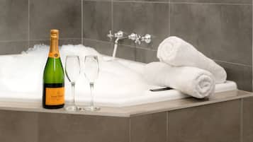A bathtub with two champagne bottles and two glasses, and two rolled towels.