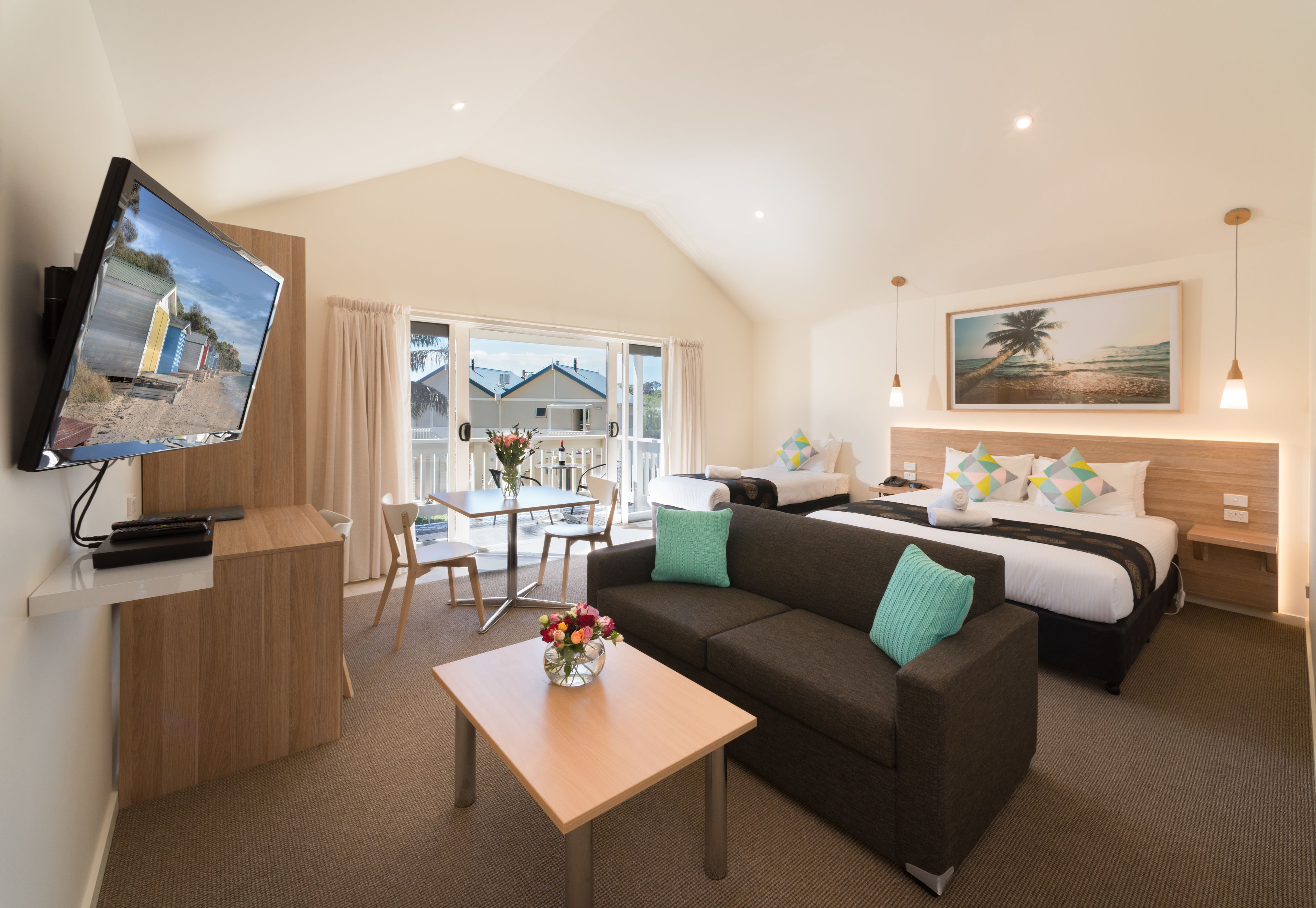 A modern hotel room with a flat-screen TV, a sofa, a dining table, and a bed.