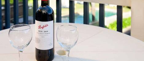 Eine Flasche Penfolds Bin 3896 Cabernet Sauvignon und zwei Weingläser auf einem weißen Tisch, im Hintergrund Grün und ein Pool zu sehen.
