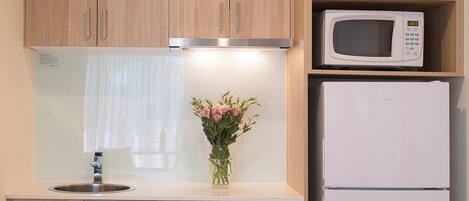Una cocina con armarios de madera, microondas, refrigerador, lavamanos y un florero con flores.