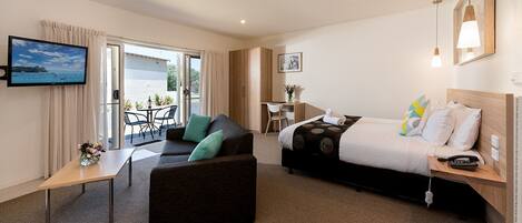 A hotel room with a bed, a sofa, a TV, a desk, and a view of the outdoors.