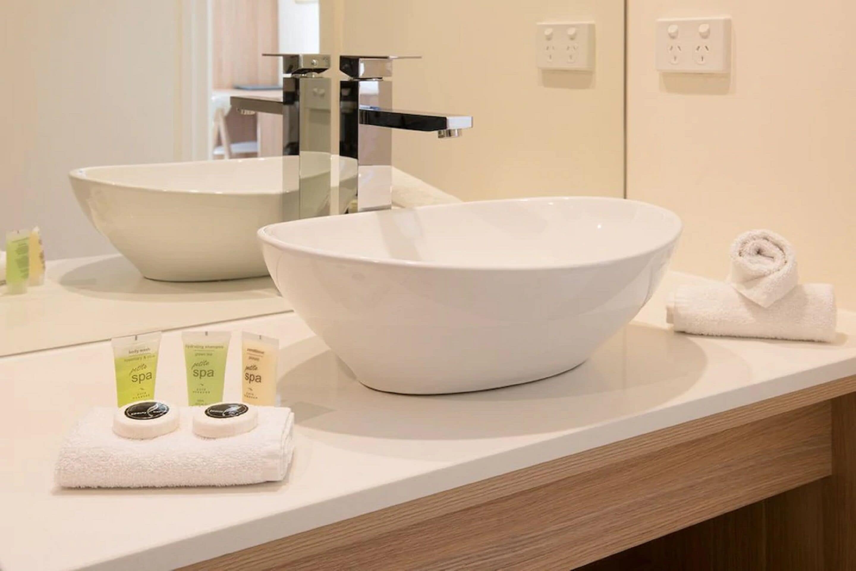 Une salle de bain avec un grand lavabo blanc, un miroir et deux flacons de produits de spa posés sur le comptoir.