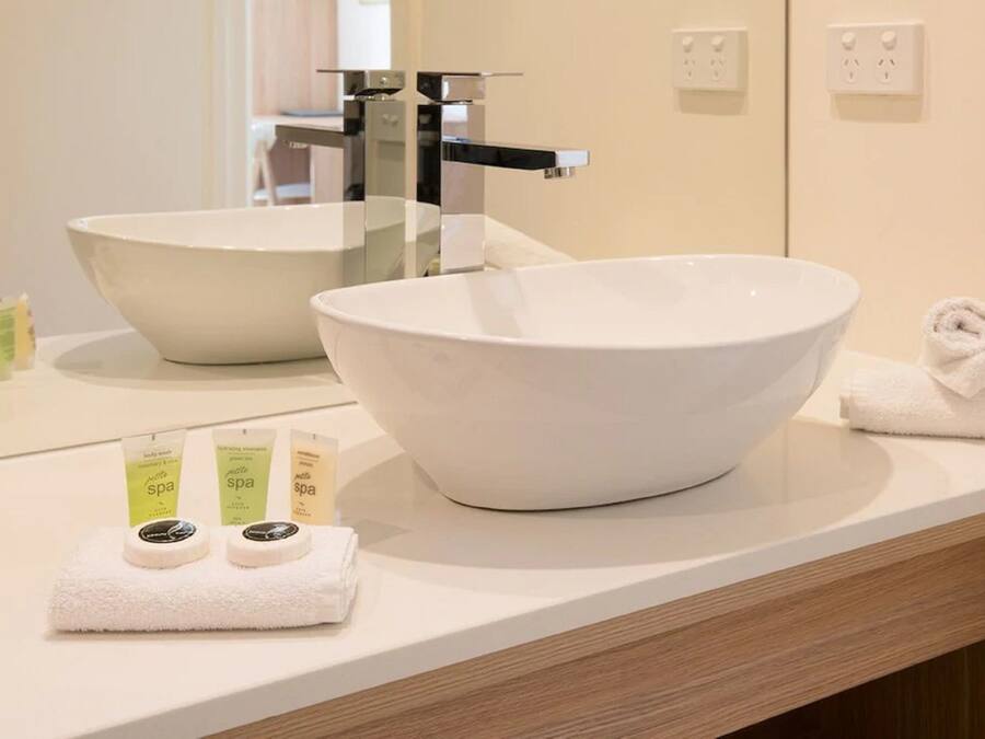 A bathroom with a large white sink, a mirror, and two spa product bottles on the counter.