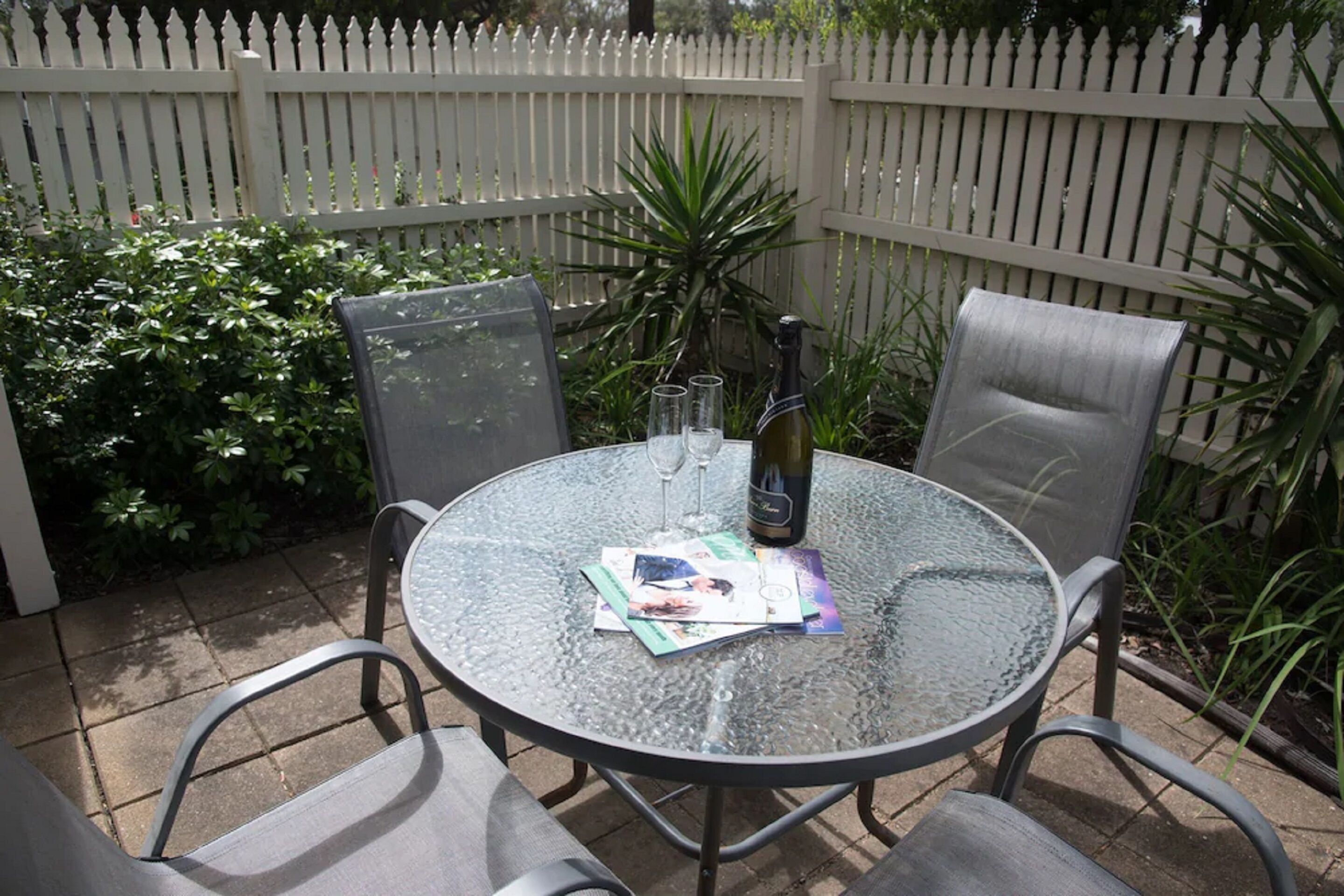 Une table ronde en verre, quatre chaises, une bouteille de vin et trois verres sont posés dessus.
