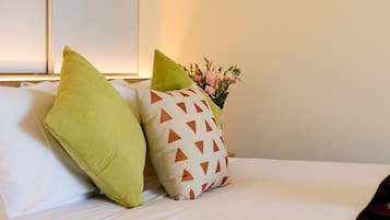 A bed with two pillows, one green and one with a geometric pattern, and a vase with flowers in the background.