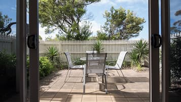 An outdoor patio with a table and chairs, surrounded by a white picket fence and various plants.