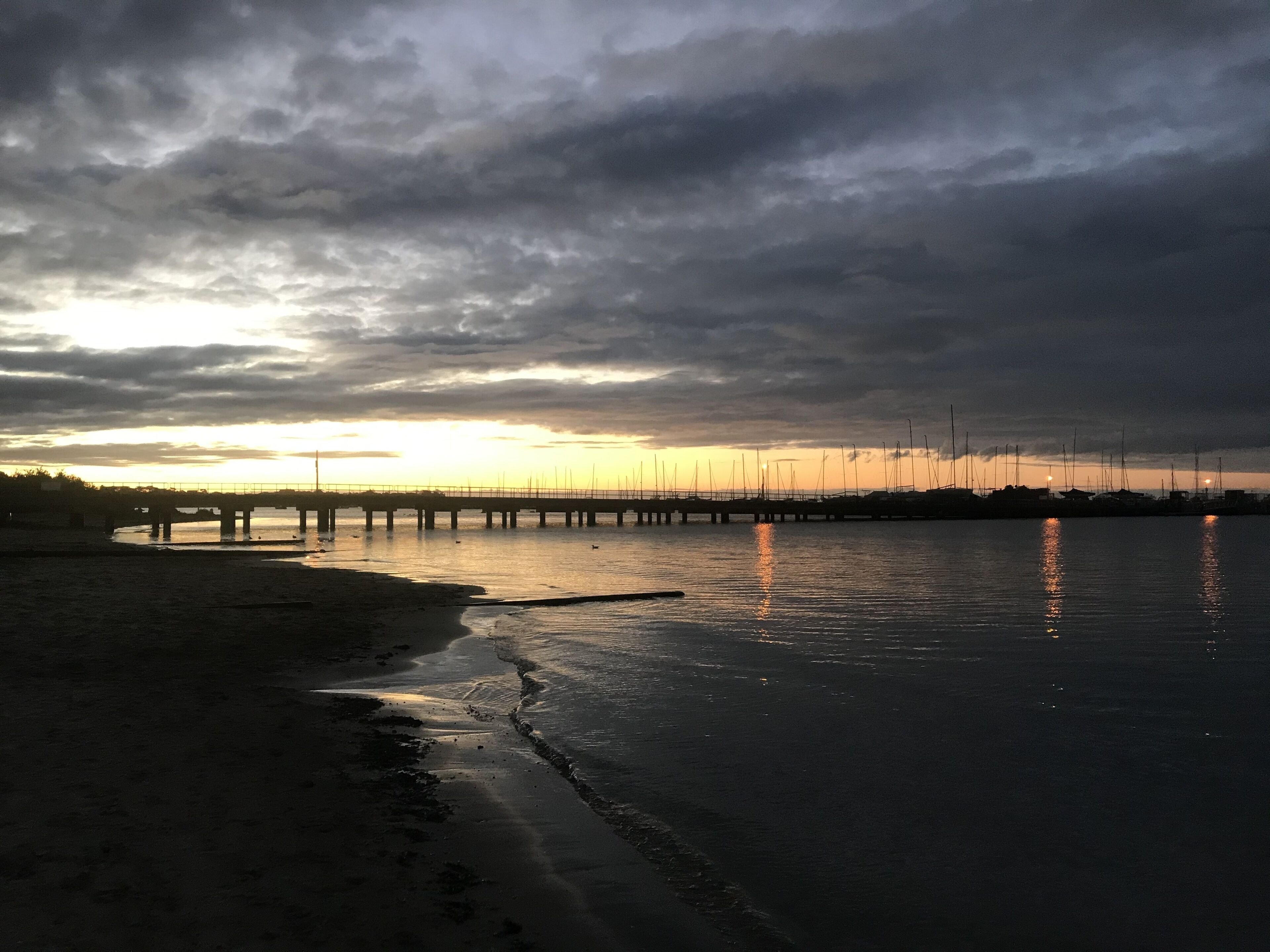 A coastal scene with a pier extending into the water, a beach in the foreground, and a sunset in the background.