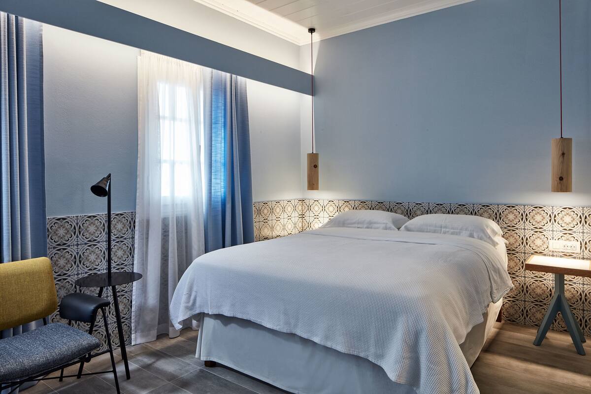 A neatly arranged bedroom with a large bed, a small table, a chair, and a hanging light fixture.