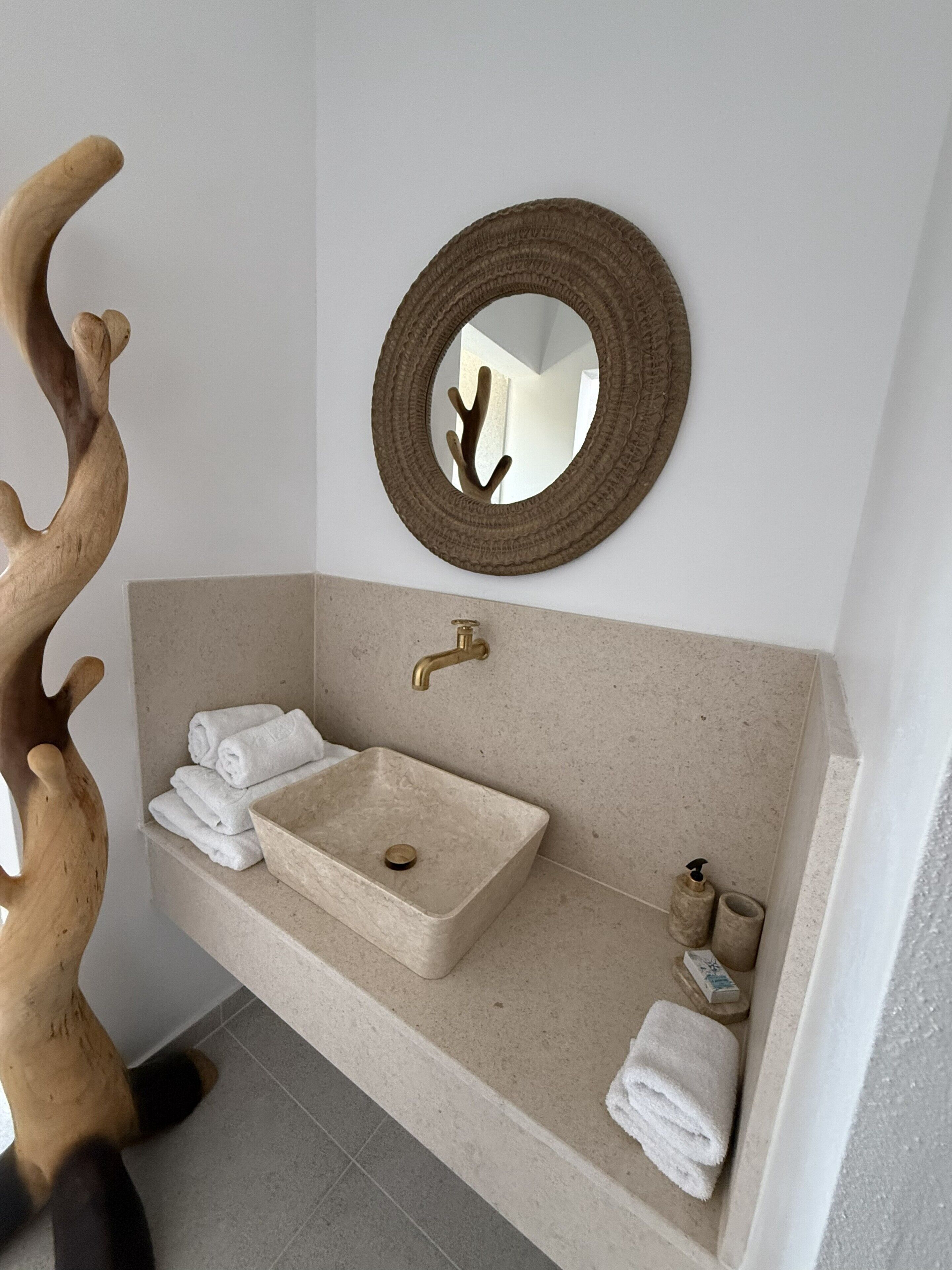 A bathroom with a beige sink, a round mirror, and a wooden decor piece.