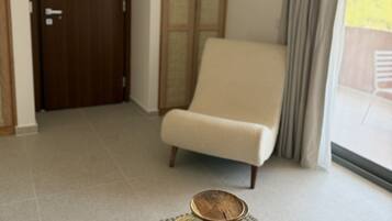 A modern living room with a wooden coffee table, a beige armchair, and a large window with curtains.