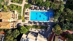 An aerial view of a resort with a central swimming pool surrounded by palm trees and a few buildings. - Angelina Aegina Boutique Escape (Aegina)