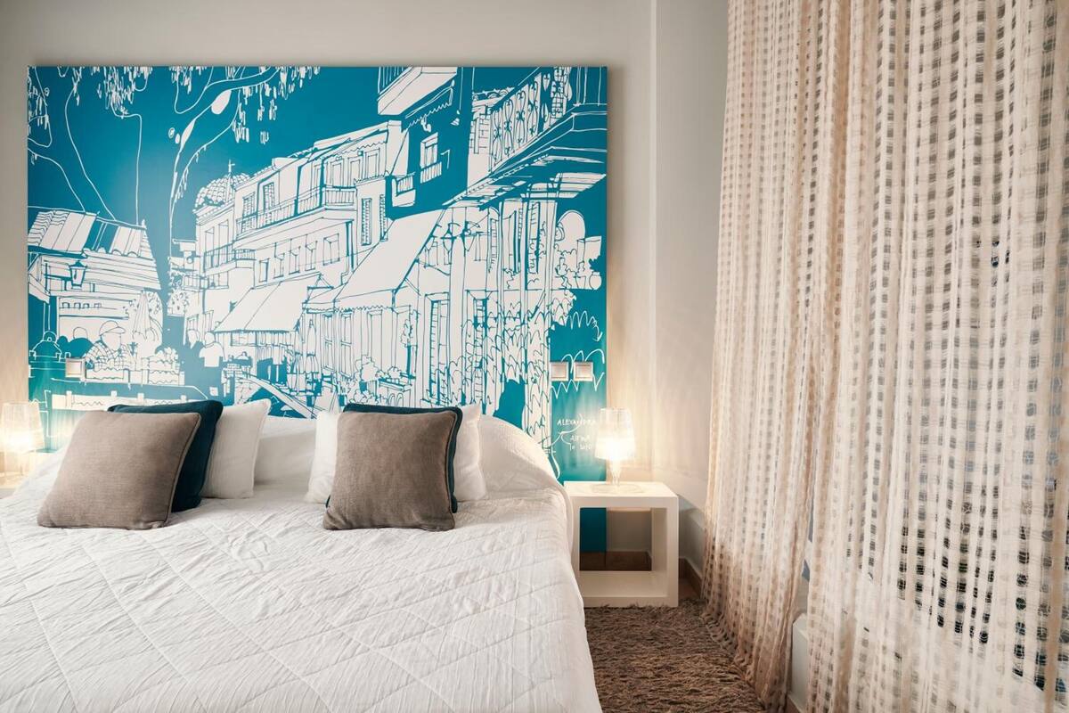 A hotel room with a large bed, two bedside tables, and a cityscape artwork on the wall.